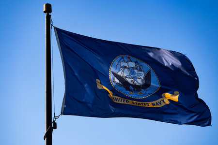 Navy flag waves beside blue sky. Outdoor navy banner supports patriotic concept. Navy heritage reflects military service tradition. Navy symbol represents american maritime authority. Military service.