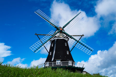 Traditional Dutch Windmill under Blue Sky with White Clouds. Classic windmill. Historic rural landmark with wooden retro windmill. Wind power for windmill.