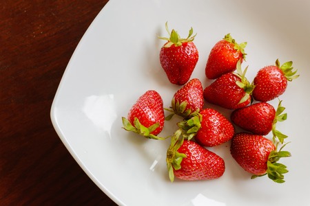 Ripe red strawberries in the plate on wooden tableの写真素材
