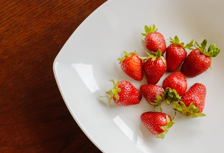 Ripe red strawberries in the plate on wooden tableの写真素材