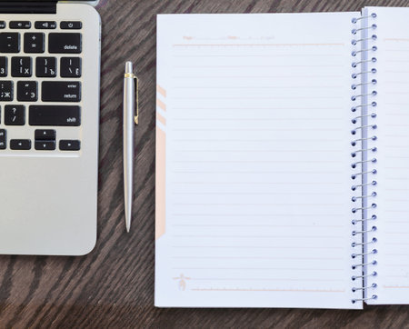 Notepad, pen and laptop on old brown wooden desk.