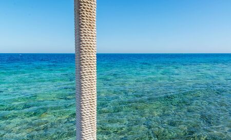 wooden pole with rope entwined on a background of blue sea and skyの写真素材