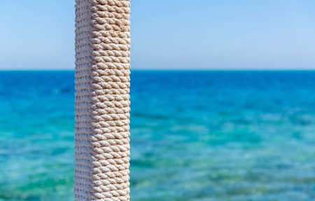 wooden pole with rope entwined on a background of blue sea and skyの写真素材