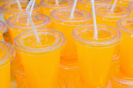 orange juice in clear cups with white strawsの写真素材