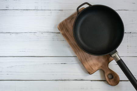 Old cast frying pan and cutting board are on the painted white wooden tableの写真素材