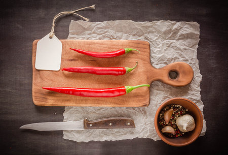 Three red fresh and sharp pepper on a cutting board. Dark background. View from above.の写真素材