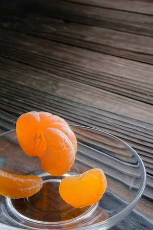 slices of orange and a ripe tangerine in a glass saucer. Against the background of the old wooden table. View angle of 45 degrees.の写真素材