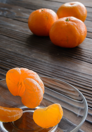slices of orange and a ripe tangerine in a glass saucer. Against the background of the old wooden table. View angle of 45 degrees.の写真素材