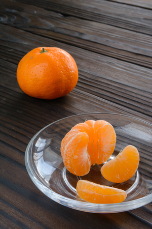 slices of orange and a ripe tangerine in a glass saucer. Against the background of the old wooden table. View angle of 45 degrees.の写真素材