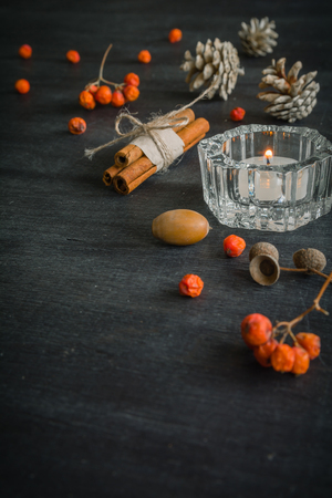 Dark Christmas background with candles and berries of mountain ash. White pine cones and branches with acorns. Cinnamon tied with string. Top view angle of 45 degrees.の写真素材