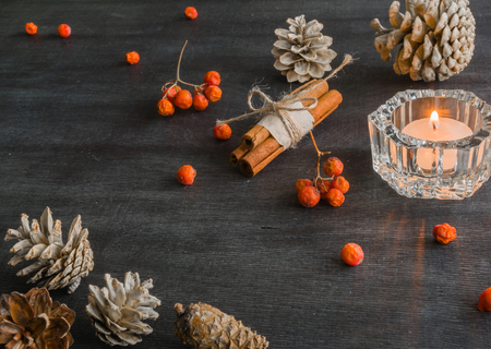 Dark Christmas background with candles and berries of mountain ash. White pine cones and branches with acorns. Cinnamon tied with string. Top view angle of 45 degrees.の写真素材