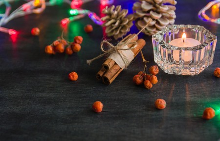 Dark Christmas background with candles and berries of mountain ash. White pine cones and branches with acorns. Cinnamon tied with string. Top view angle of 45 degrees.の写真素材