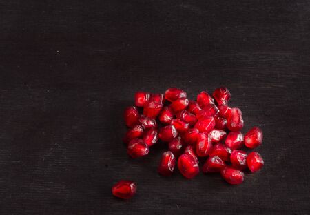 Red juicy ripe pomegranate grains on dark wooden background.の写真素材