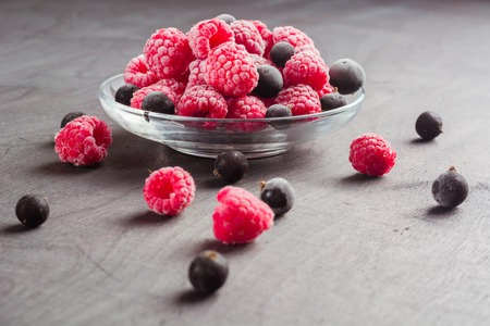 Frozen raspberries in a glass saucer. Frost on the berries. Dark background.の写真素材