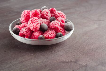 Frozen raspberries in a glass saucer. Frost on the berries. Dark background.の写真素材