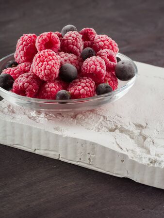 Frozen raspberries in a glass saucer. Frost on the berries. Dark background.の写真素材