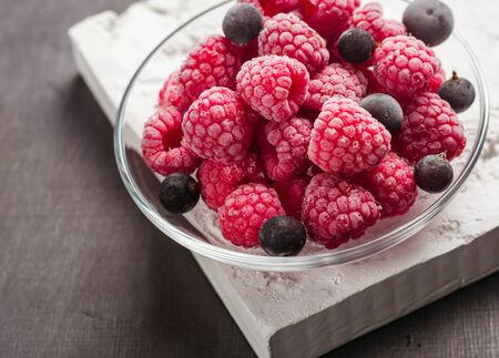 Frozen raspberries in a glass saucer. Frost on the berries. Dark background.の写真素材