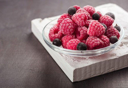 Frozen raspberries in a glass saucer. Frost on the berries. Dark background.の写真素材