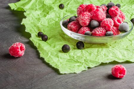Frozen raspberries in a glass saucer. Frost on the berries. Dark and green background. Green crumpled paper.の写真素材