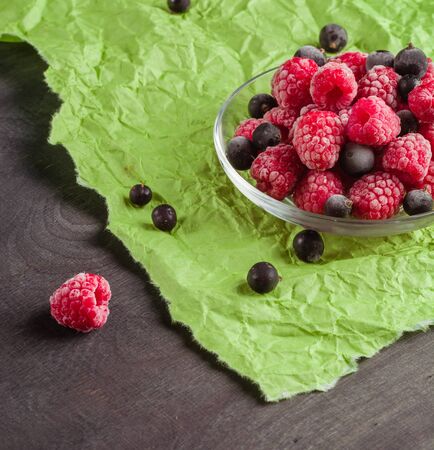 Frozen raspberries in a glass saucer. Frost on the berries. Dark and green background. Green crumpled paper.の写真素材