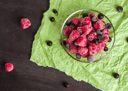 Frozen raspberries in a glass saucer. Frost on the berries. Dark and green background. Green crumpled paper.の写真素材