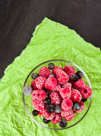 Frozen raspberries in a glass saucer. Frost on the berries. Dark and green background. Green crumpled paper.の写真素材