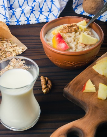 Cooked porridge oatmeal in a bowl on a wooden dark background. Ingredients for cooking. Milk and napkin.の写真素材