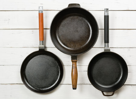 Several empty cast-iron frying pans on a white wooden background. View from above. Space for text.の写真素材