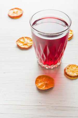 Hibiscus tea in a glass mug on a wooden table among rose petals and dry tea custard. Copy space.の写真素材