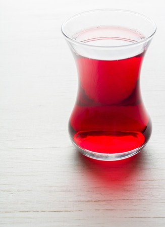 Hibiscus tea in a glass mug on a wooden table among rose petals and dry tea custard. Copy space.の写真素材