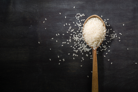 A handful of white polished rice in a wooden old spoon. Dark wood background. View from above. Space for text.の写真素材