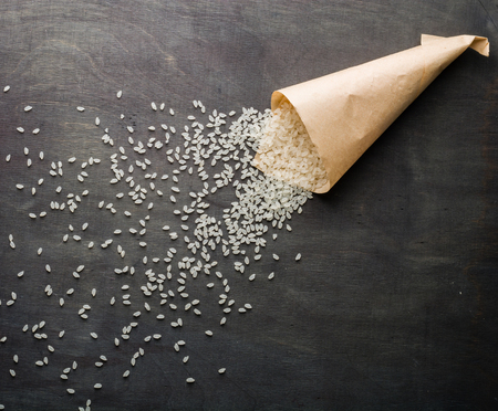 White rice scattered over the dark wooden table of a paper bag. View from above. Space for text.の写真素材