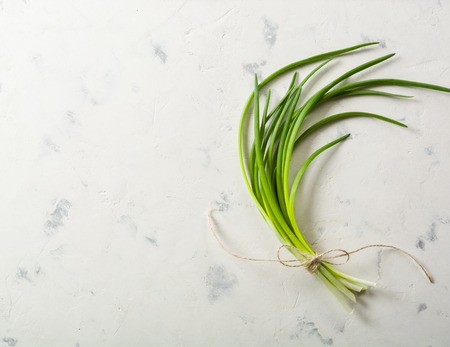 A bunch of green spring onions tied with a rope on a light stone background. Space for text. View from above.の写真素材