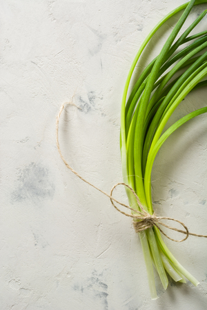 A bunch of green spring onions tied with a rope on a light stone background. Space for text. View from above.の写真素材