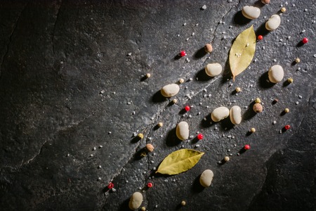 White beans and spices are scattered randomly on a black stone table from slate. Space for text.の写真素材
