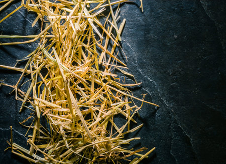 A bunch of yellow straw on the black background of an empty slab of slate. Place for text.