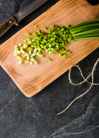 A bunch of green onions on a cutting board. Background black slate.の写真素材