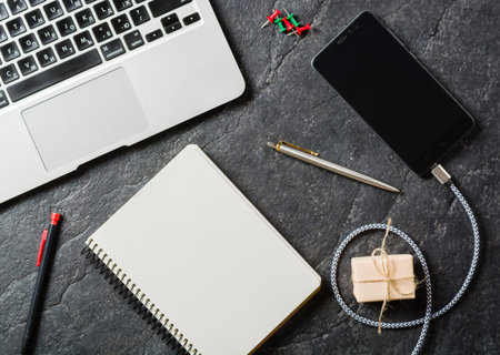 Business background with laptop and notepad on black stone background. Empty page.