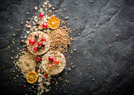 Round Crisp on a black stone background. Rice grains, oatmeal flakes and buckwheat series. Berries and fruit top.の写真素材