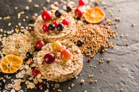 Round Crisp on a black stone background. Rice grains, oatmeal flakes and buckwheat series. Berries and fruit top.の写真素材
