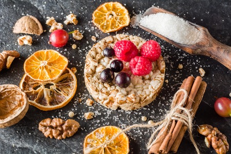 Round Crisp on a black stone background. Rice grains, oatmeal flakes and buckwheat series. Berries and fruit top.の写真素材