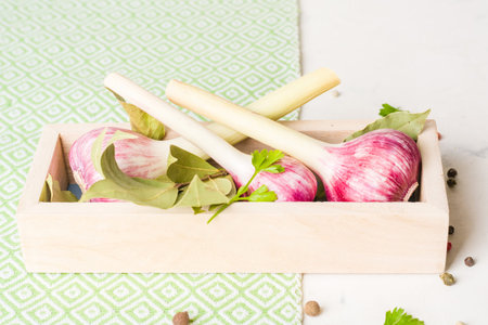 Garlic purple with Parsley in wooden box on a white stone background. A lot of empty space.