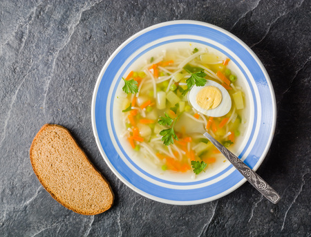 Soup with egg, pasta and vegetables in a blue plate on a black background. Place for text.の写真素材
