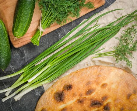 A large loaf of bread with green onions and dill on a black background. View from above.の写真素材