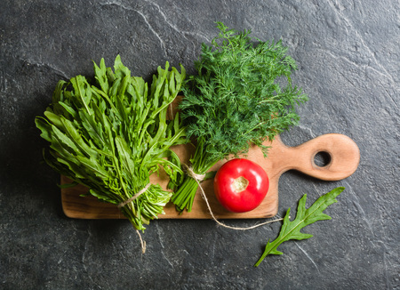 Tomato and two bunches of green on a black background. A lot of empty space.の写真素材