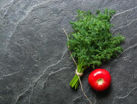 Tomato and two bunches of green on a black background. A lot of empty space.の写真素材