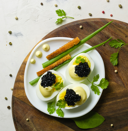 Appetizer of eggs, white sauce and black caviar. Layout on a wooden background with spices and herbs. View from above.の写真素材
