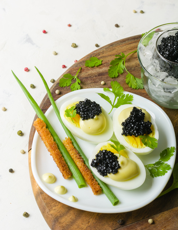 Appetizer of eggs, white sauce and black caviar. Layout on a wooden background with spices and herbs. View from above.の写真素材