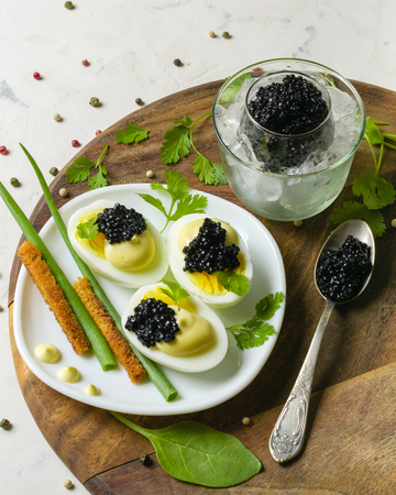 Appetizer of eggs, white sauce and black caviar. Layout on a wooden background with spices and herbs. View from above.の写真素材