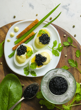 Appetizer of eggs, white sauce and black caviar. Layout on a wooden background with spices and herbs. View from above.の写真素材